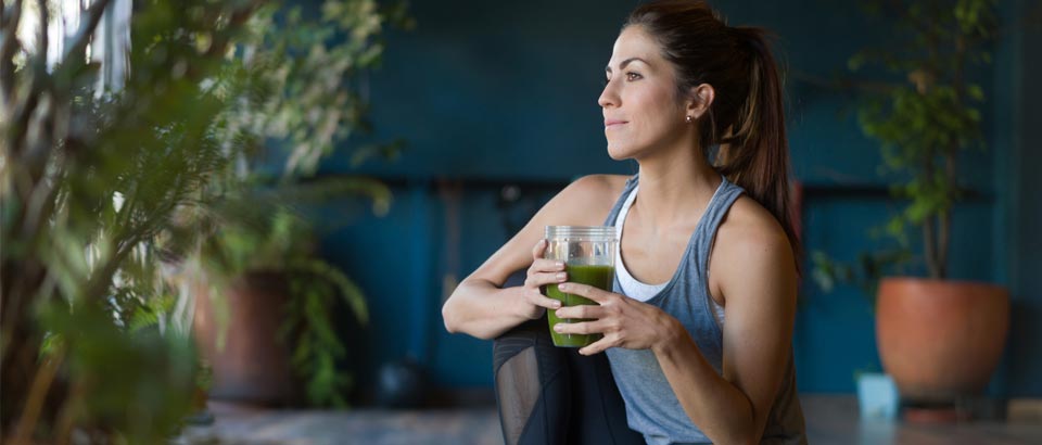 woman in gym clothes drinking green smoothie