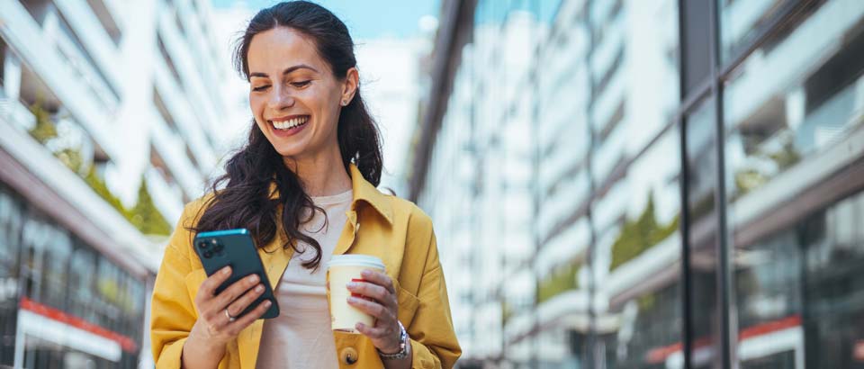 woman smiling with coffee looking at her phone