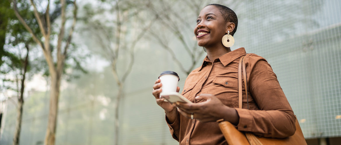 woman smiling and holding phone and disposable coffee cup in middle of foggy forest