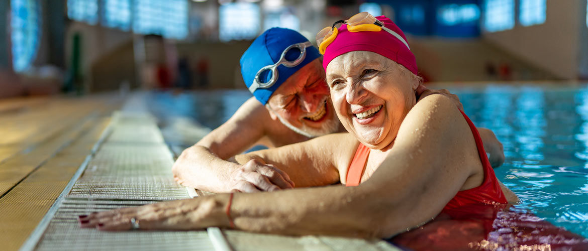 older woman wading and holding onto edge of pool wearing a pool cap