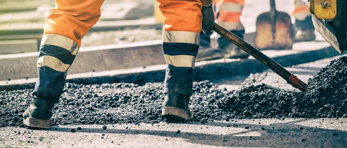 close up image of somone laying asphalt with work boots on