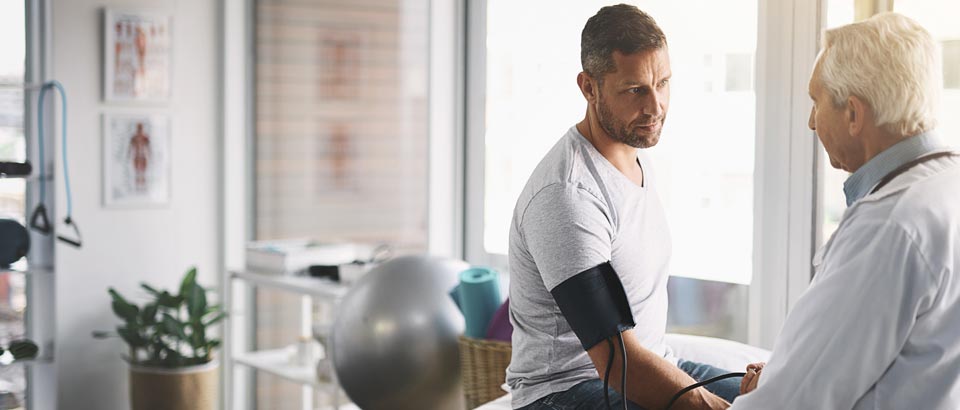 doctor taking blood pressure of man sitting on exam table