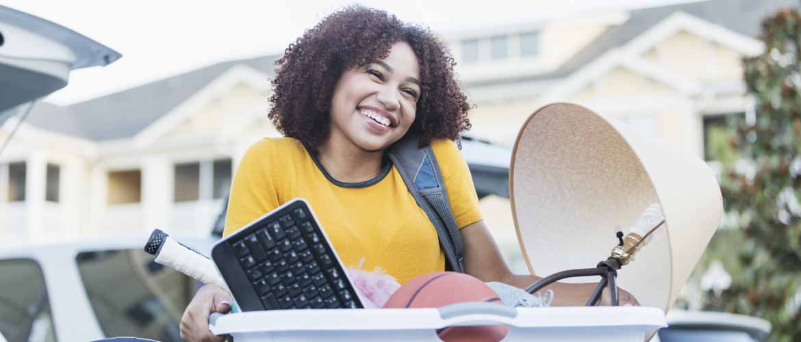 a girl holding a laundry basket full of items for college