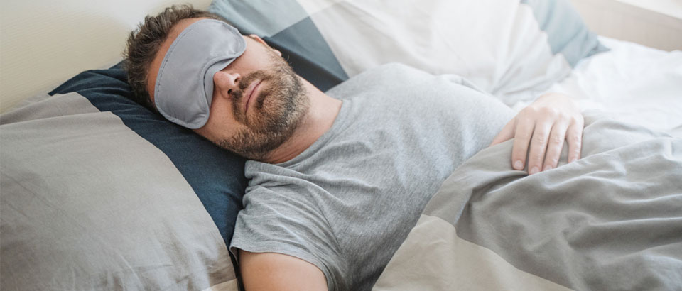 man sleeping in bed with an eye mask