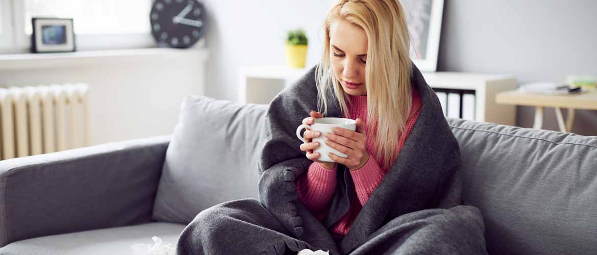 a woman sitting on a couch wrapped in a blanket holding a cup of tea