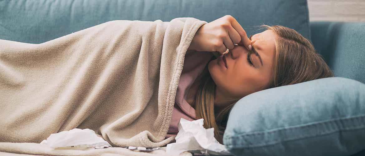 a woman lying on a couch pinching the skin between her eyes with tissues beside her