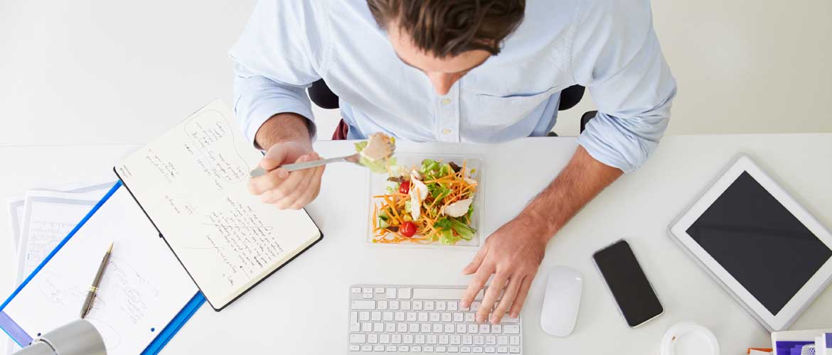 man eating a salad at his work desk