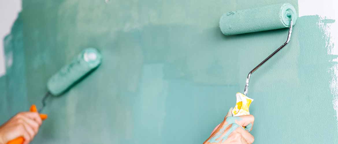 close-up of two people's hands using a paint roller to paint a wall turquoise