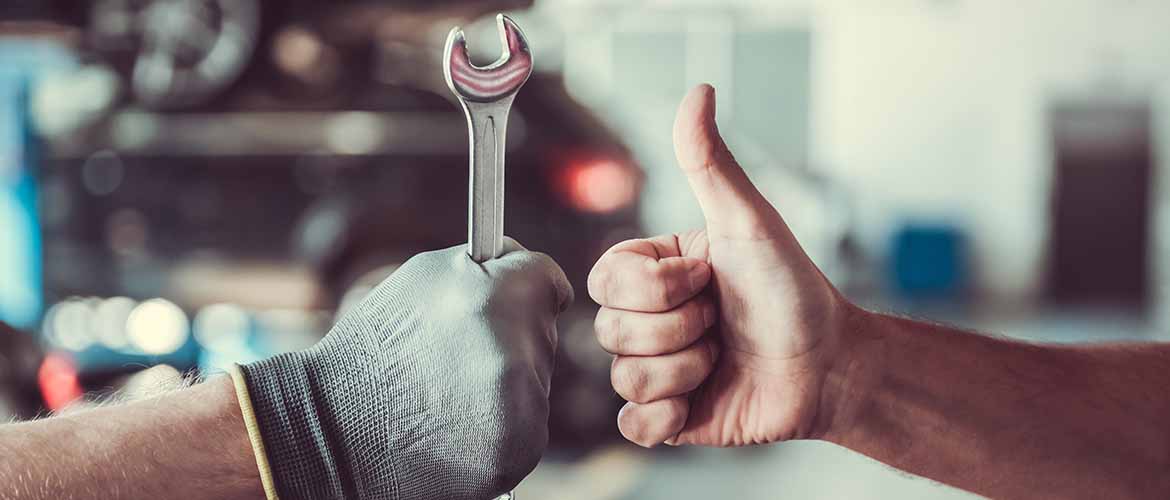 two mechanics working in auto service. One is holding a spanner, while the other is giving a thumbs up