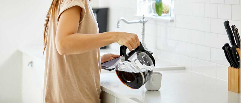 a woman pouring a cup of coffee while scrolling on her phone