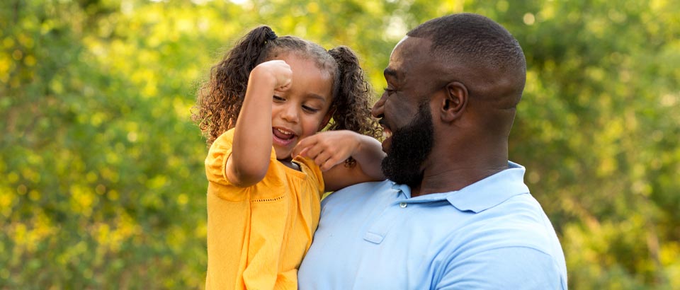 father holding daughter while she shows him her arm muscle