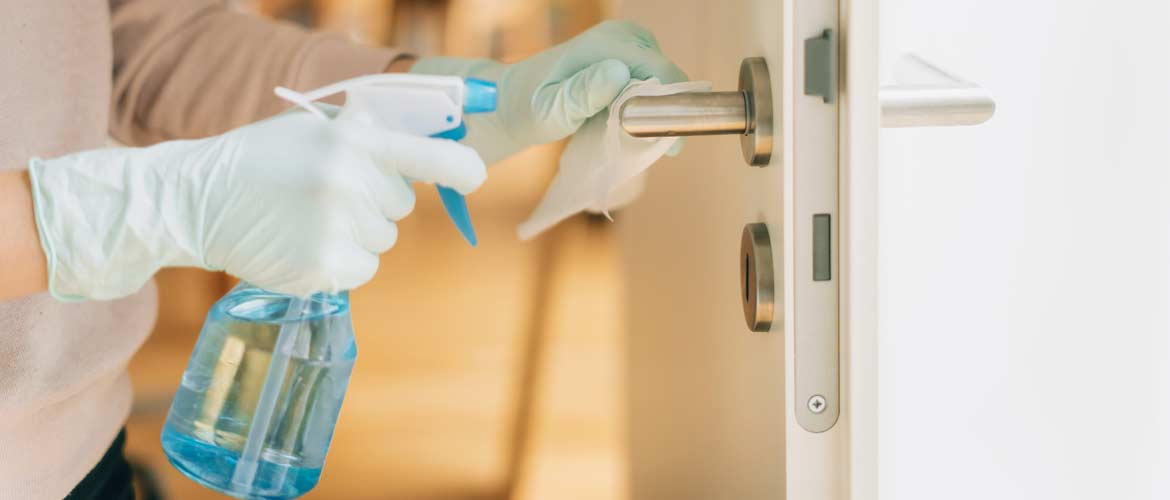 a person wearing gloves disinfecting a door handle with cleaner