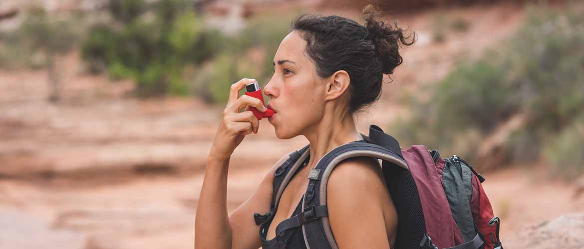 woman using an inhaler while out hiking