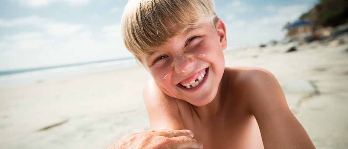 young boy with sunscreen on his face smiling while at the beach