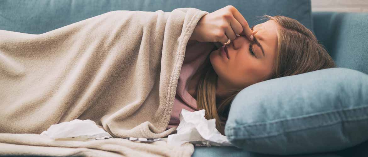 a sick woman lying on a couch with her hand on her hand and tissues beside her