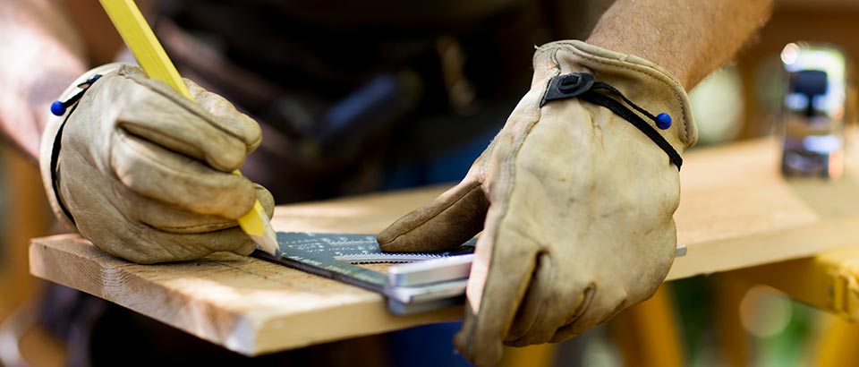 a person wearing gloves marking a measurement on a piece of wood