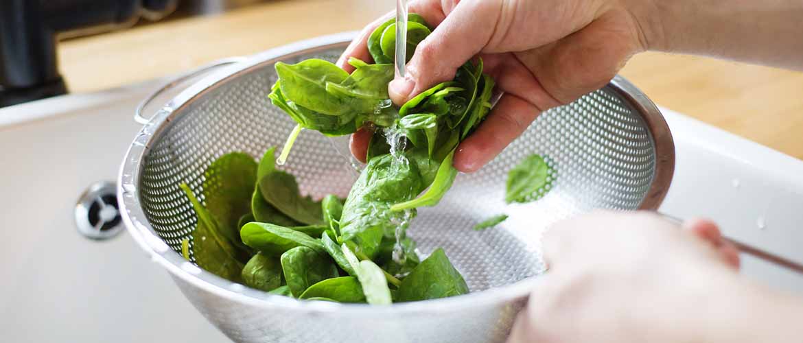 a person washing spinach in a colander in a sink