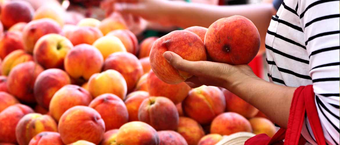 a woman holding three peaches while shopping at a grocery store