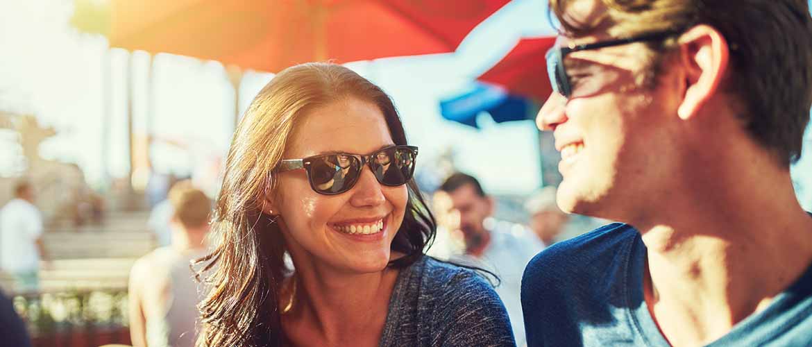 a woman and man wearing sunglasses outside smiling at each other