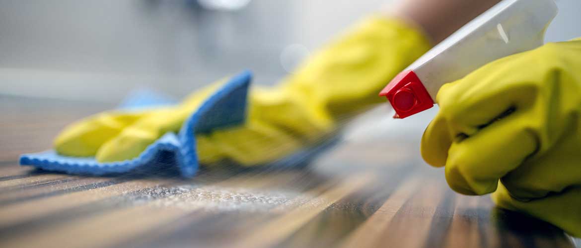 A person wearing gloves and holding a sponge and spray bottle wiping a table