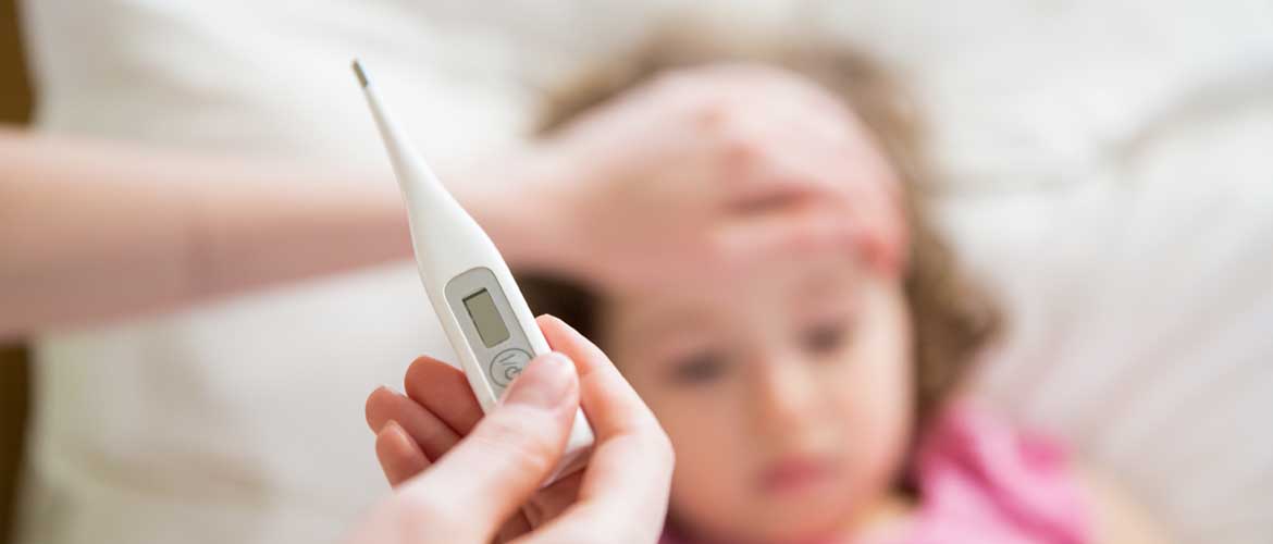 A hand holding a thermometer and another hand on the forehead of a small child lying down