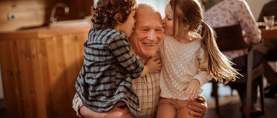 a grandfather holding a little boy and girl on his legs as each give him a kiss