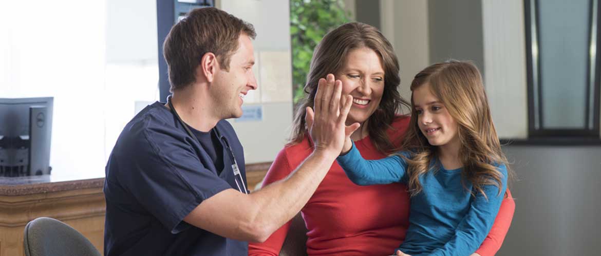 A girl sitting on her mom's lap, giving the doctor a high five