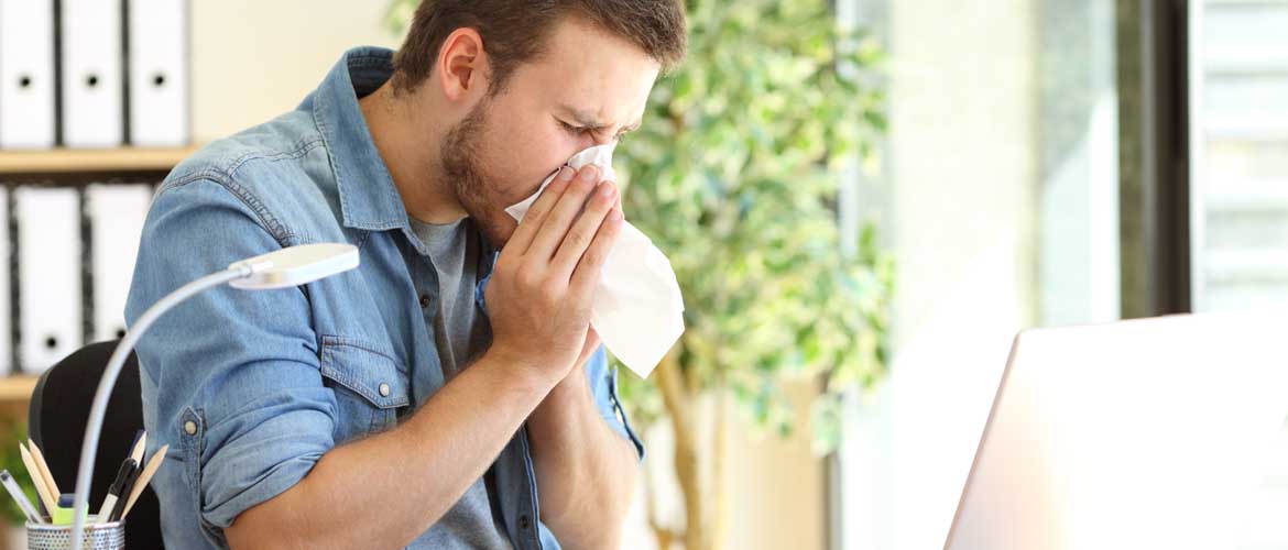 A man at his desk blowing his nose