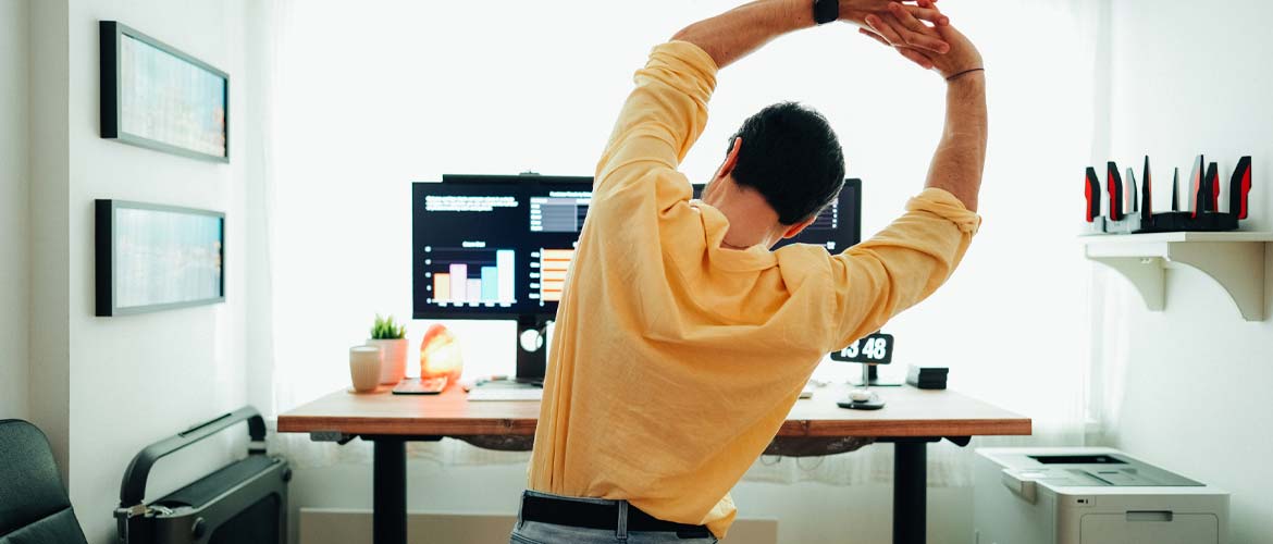 man stretching in front of computer at home